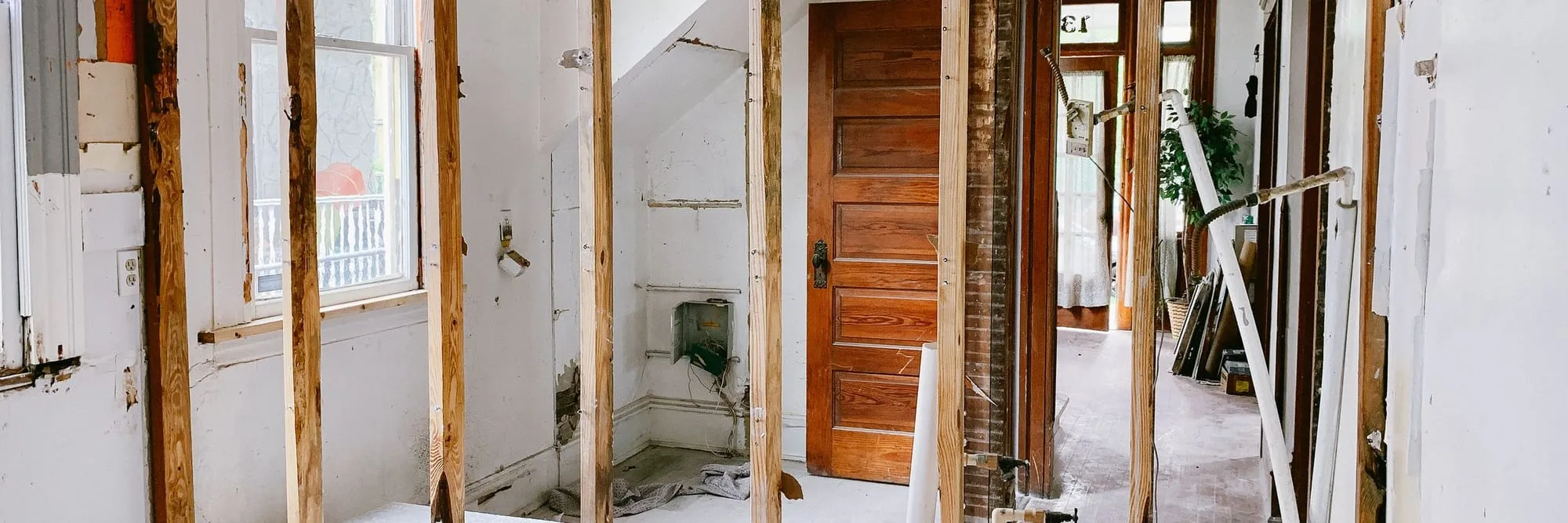 The interior of a house part-way through renovation, stripped back to bare studs with a sightline through a doorway into the hallway beyond.